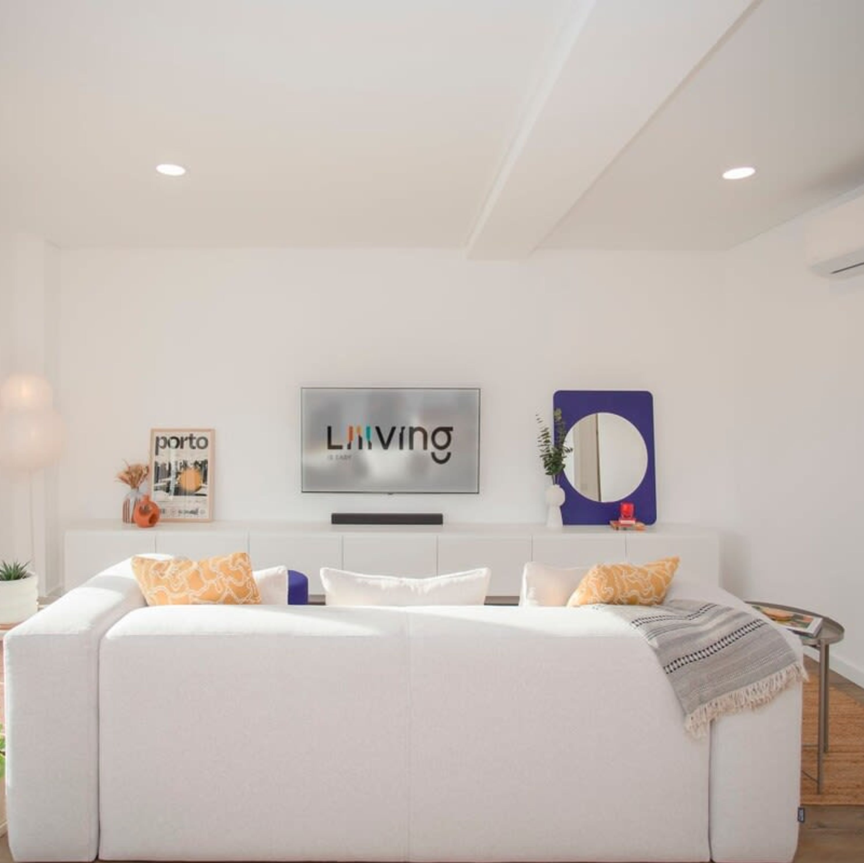 Ein modernes Wohnzimmer mit einem weißen Sofa, einem Flachbildfernseher und einem gerahmten Kunstwerk an der Wand.