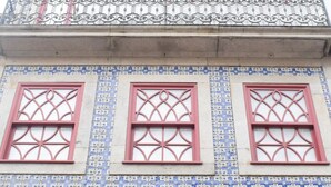 Un bâtiment dont la façade est ornée de carreaux bleus et blancs, avec des encadrements de fenêtres rouges et des éléments décoratifs en fer forgé sur le balcon.