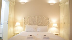 Un lit bien fait, avec du linge de lit et des serviettes blanches, deux lampes de chevet et une tête de lit en métal au style classique.