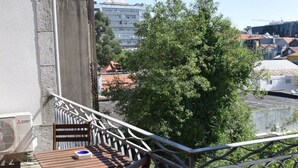 Un balcon avec une table et des chaises, donnant sur un quartier résidentiel bordé d’arbres et comprenant des immeubles.