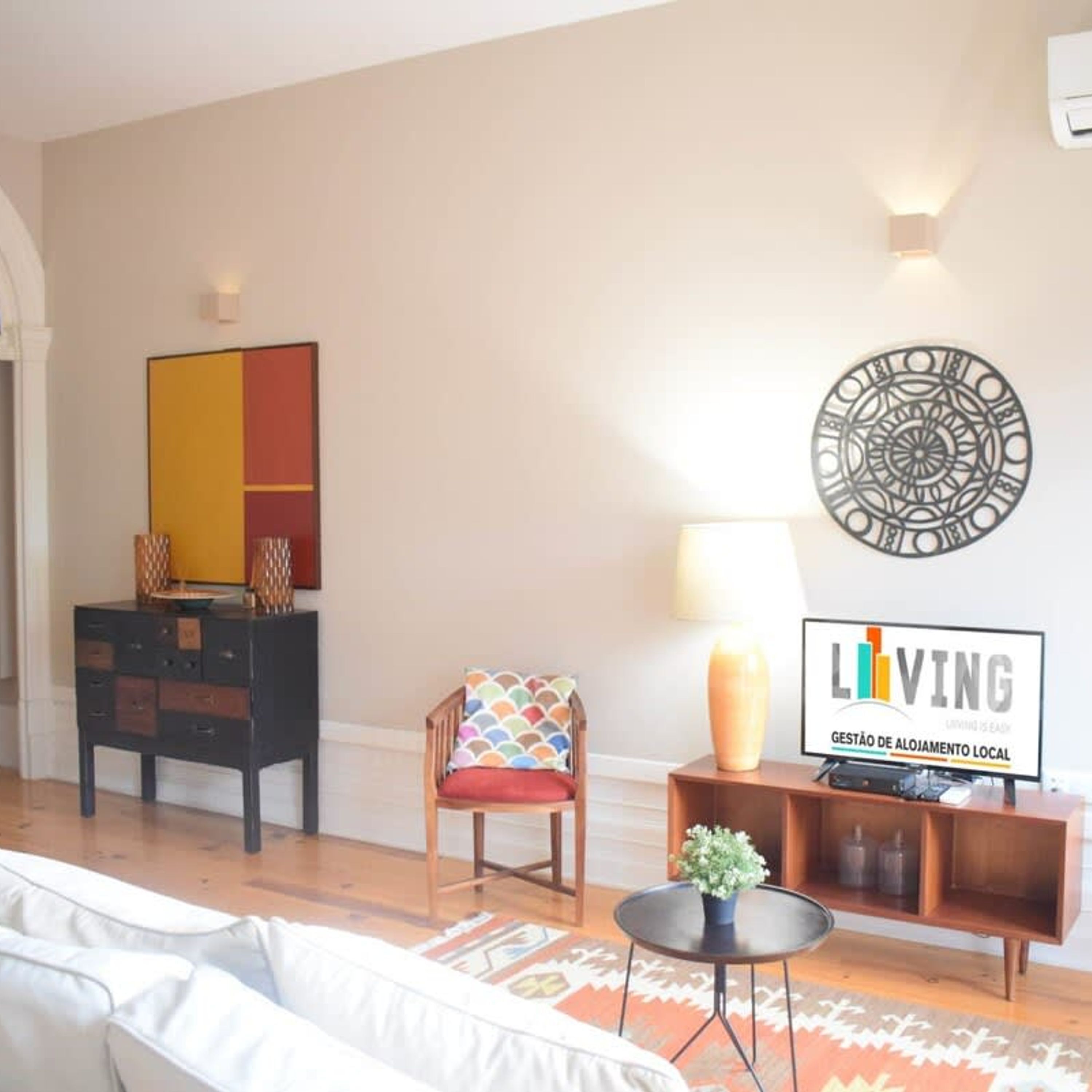 Een woonkamer met een bank, een stoel, een salontafel, een kast en een wand met een rond kunstwerk en een bord.