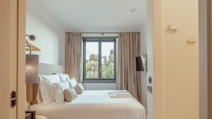 A bedroom with a large bed, a bedside table with a lamp, a window with curtains, and a TV mounted on the wall. - Liiiving in Porto - Casa Duque Apartment III (Porto)