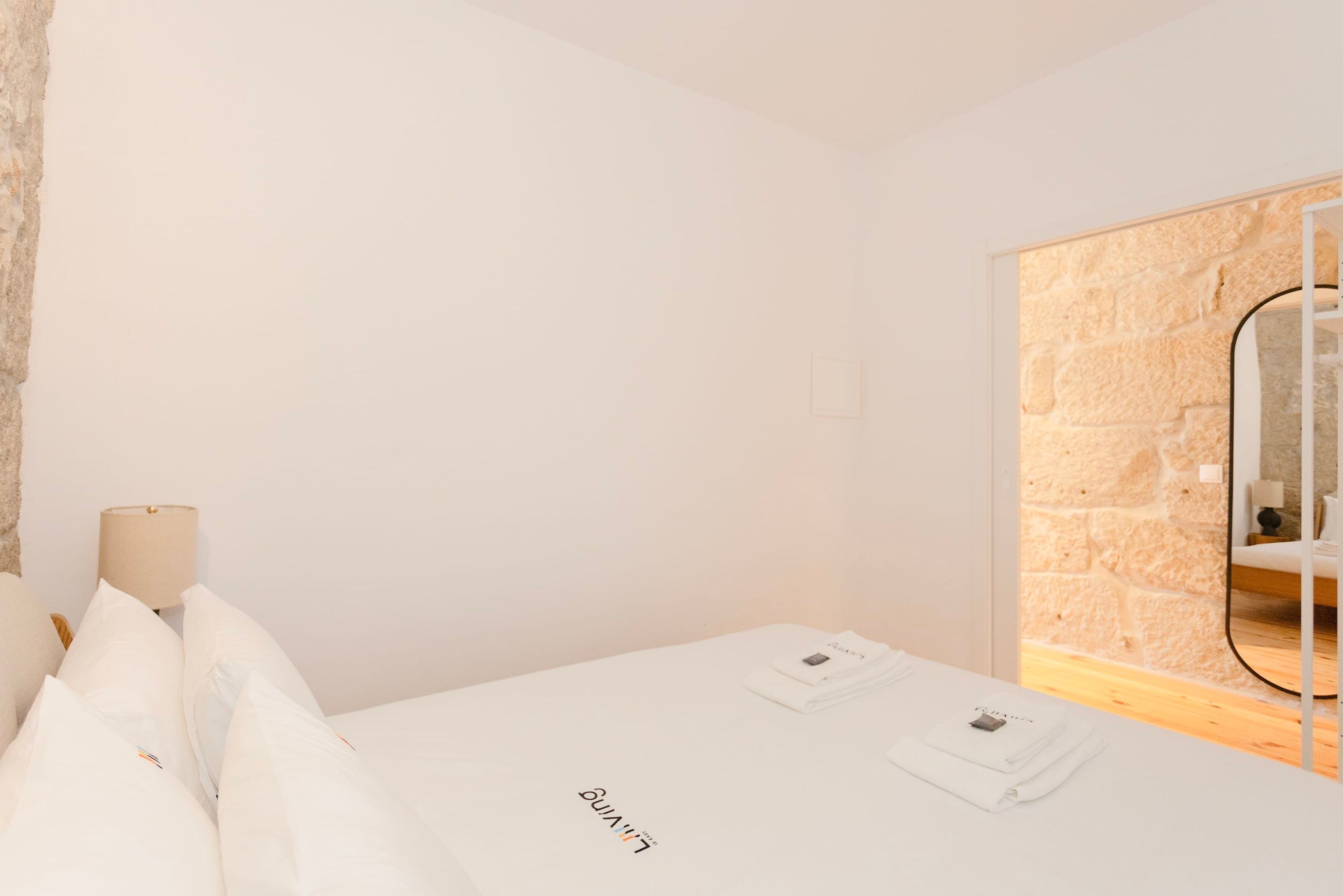 A hotel room with a bed, a lamp, a mirror, and a stone wall.