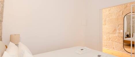 A hotel room with a bed, a lamp, a mirror, and a stone wall.