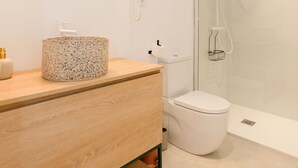 A modern bathroom with a wooden vanity, a round mirror, a toilet, and a glass-enclosed shower area. - Liiiving In Gaia - The Wine Side V (Vila Nova de Gaia)