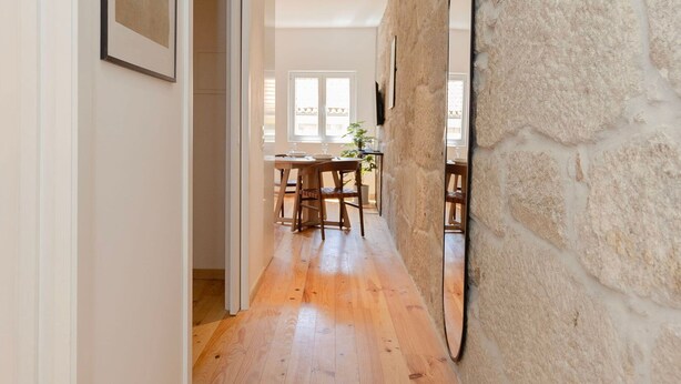 A hallway with wooden flooring, a stone wall, and a mirror. There is a dining area visible in the background. - Liiiving In Gaia - The Wine Side V (Vila Nova de Gaia)