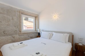 A bedroom with a stone wall, a window, a bed with white bedding, and a bedside lamp. - Liiiving In Gaia - The Wine Side XIV (Vila Nova de Gaia)