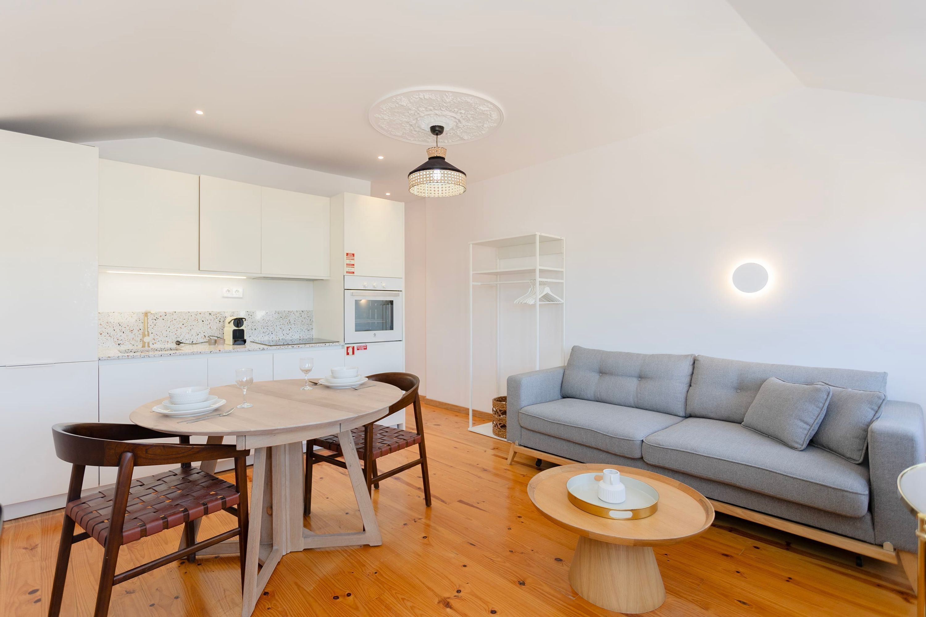 A modern living room with a grey sofa, wooden dining table, and chairs.