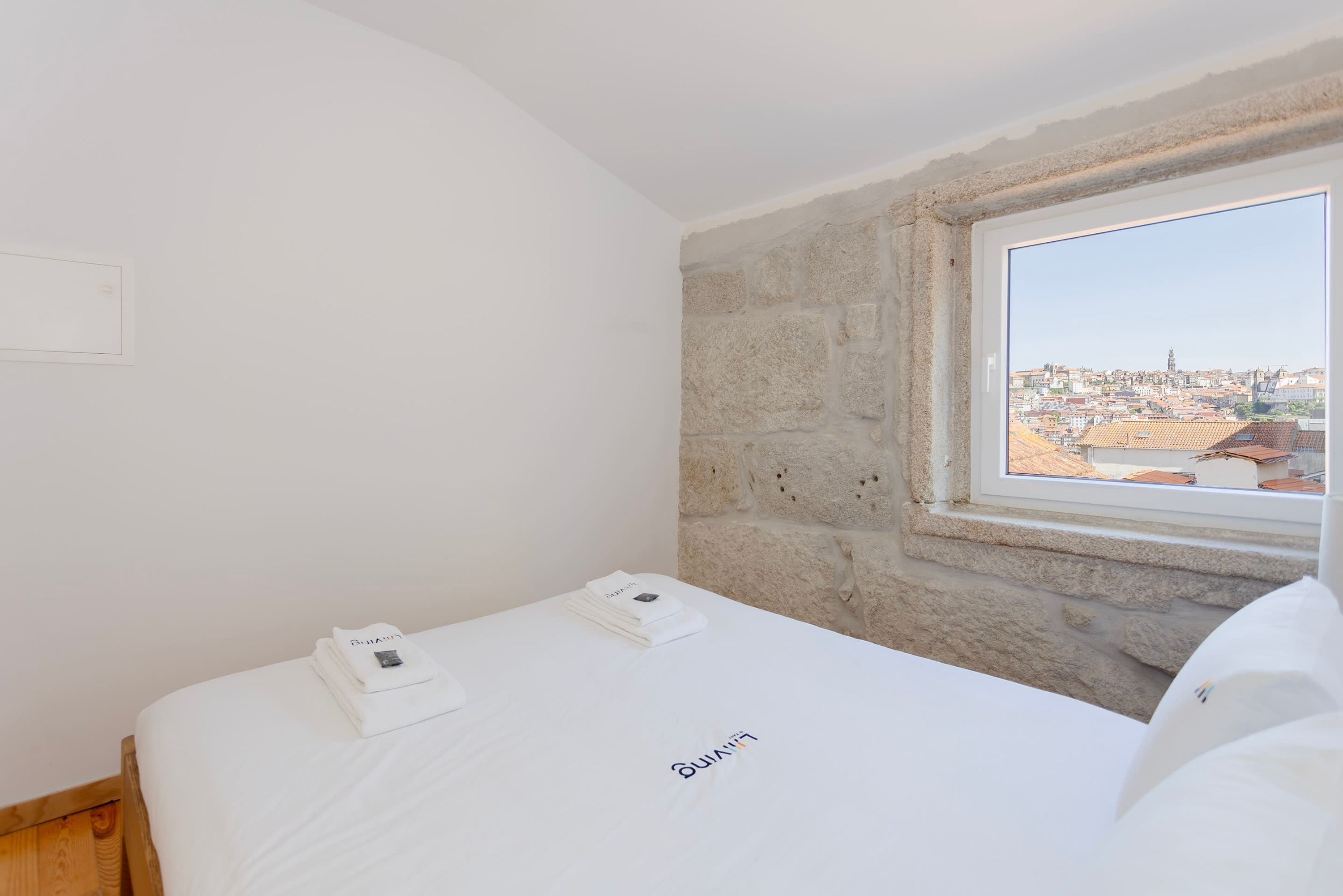 Ein Hotelzimmer mit Bett, Fenster und Blick auf die Stadt sowie einer Steinwand.