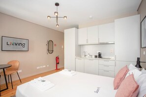 A modern hotel room with a bed, a small table, a chair, a kitchenette, and a ceiling light fixture. - Liiiving in Porto Historic Cl Rigos Studio - 3F (Porto)