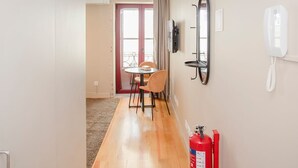 A hallway with a wooden floor, a dining area with a table and chairs, a red fire extinguisher, a mirror, and a phone on the wall. - Liiiving in Porto Historic Cl Rigos Studio - 3F (Porto)