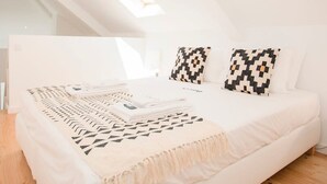 Ein modernes, weißes Schlafzimmer mit Dachfenster, einem Bett mit gemusterten Kissen und ordentlich bezogenem Bett.