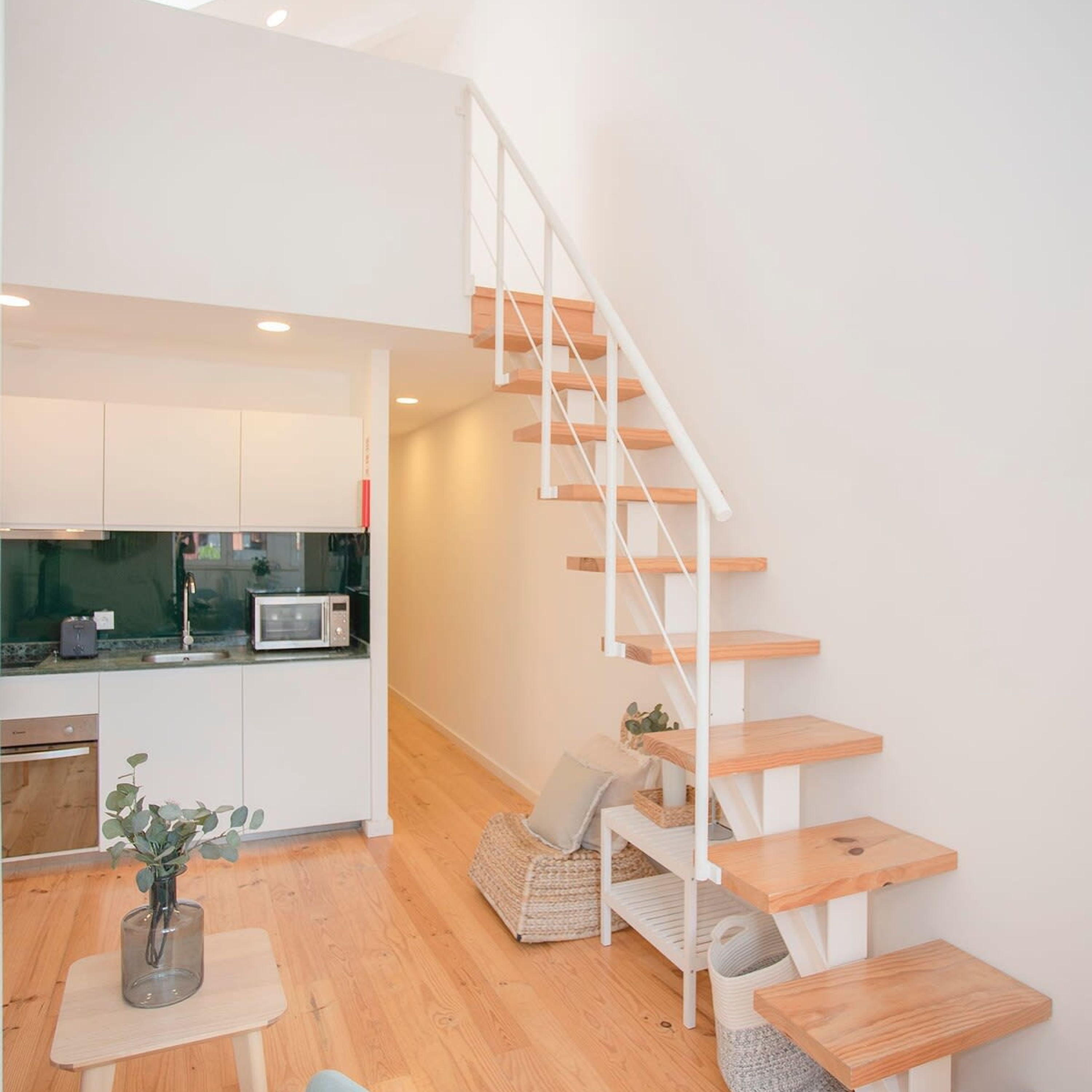 Une cuisine moderne avec des armoires blanches, un four à micro-ondes et un évier. Un escalier en bois, doté d’une rampe blanche, mène à un niveau inférieur.