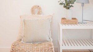 Eine gemütliche Ecke mit einem gewebten Stuhl, Kissen, einem kleinen Tisch mit Lampe und einer Pflanze.