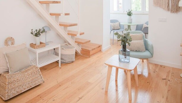 Ein modernes Wohnzimmer mit einer Holztreppe, einem kleinen Tisch mit einer Vase und einem blauen Sessel.