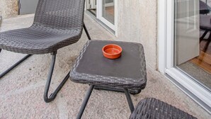 Un balcone con mobili in vimini, un tavolino con una ciotola e una porta scorrevole in vetro.