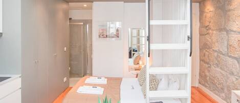 A modern loft apartment with a loft bed, a dining area with a plant, and a stone accent wall.