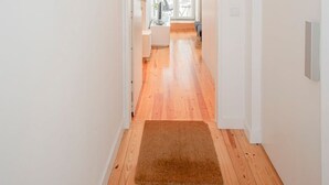 Un corridoio con pavimento in legno e pareti bianche, che conduce a una stanza con una porta bianca e vista all'esterno.