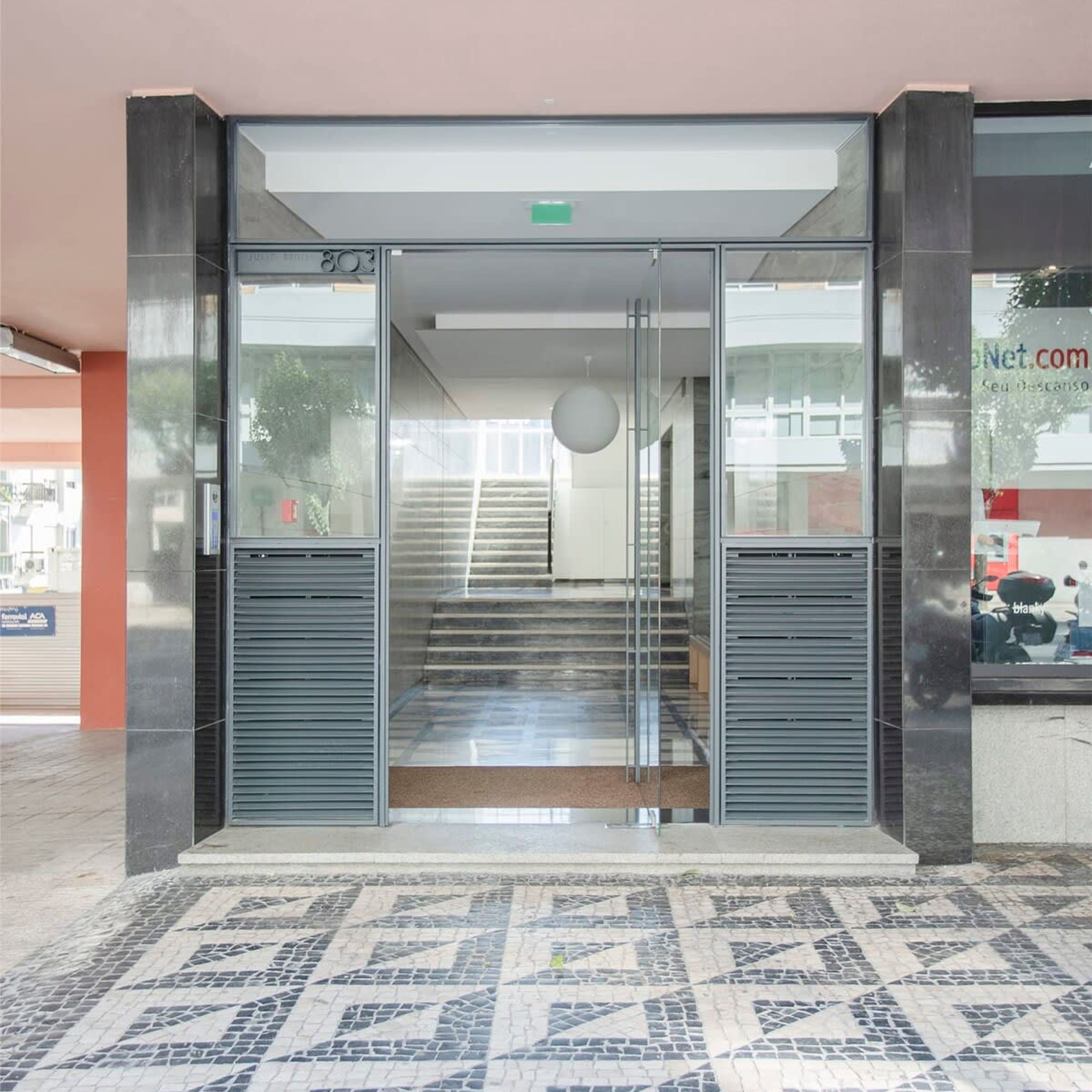 A modern building entrance with a glass door, a staircase leading inside, and a tiled floor.