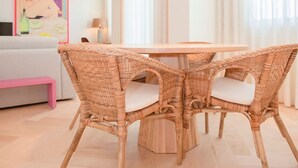 Un comedor con una mesa redonda y cuatro sillas de mimbre con cojines blancos.