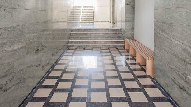 Un pasillo moderno con piso a cuadros, paredes de mármol y una escalera que sube a un nivel superior.