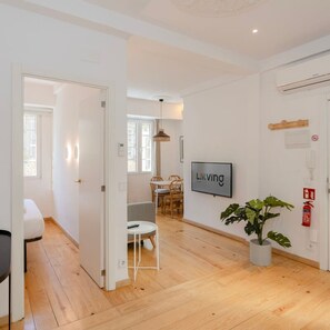 Eine moderne Wohnung mit Essbereich, Wohnzimmer mit Fernseher und einer großen Topfpflanze.