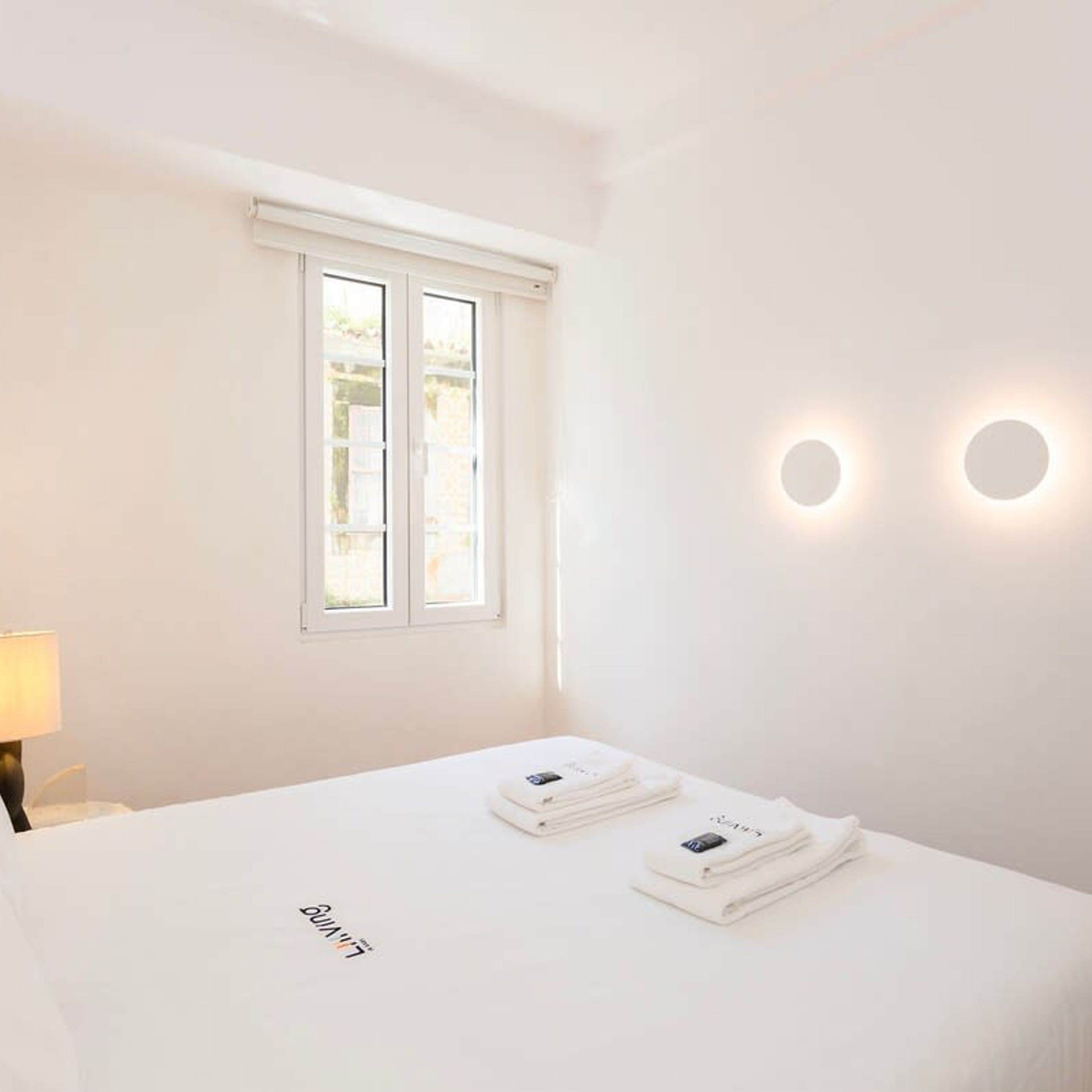Une chambre d’hôtel avec un lit, une fenêtre et deux lampes fixées au mur.