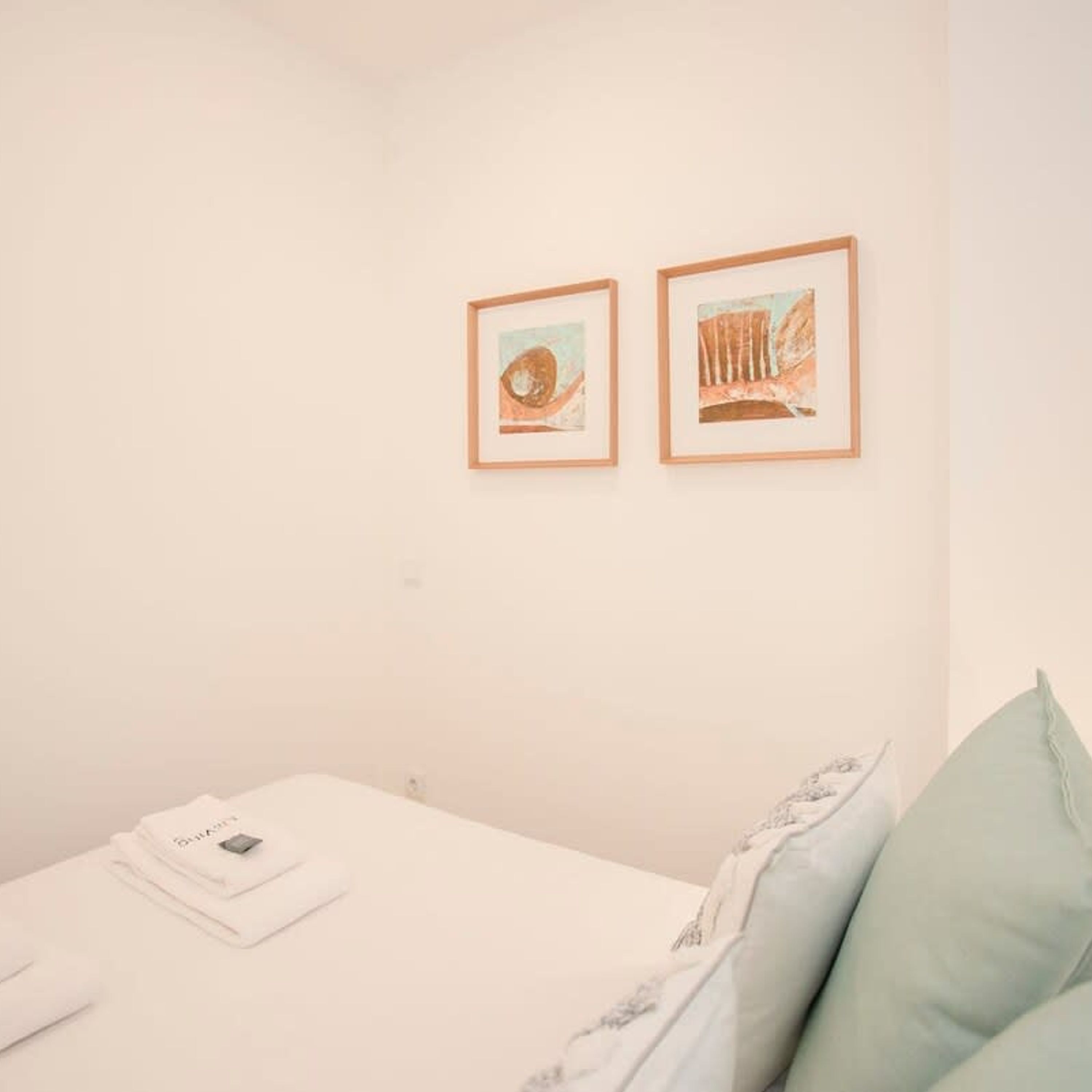 A minimalist room with a bed, a pillow, and two framed artworks on the wall.