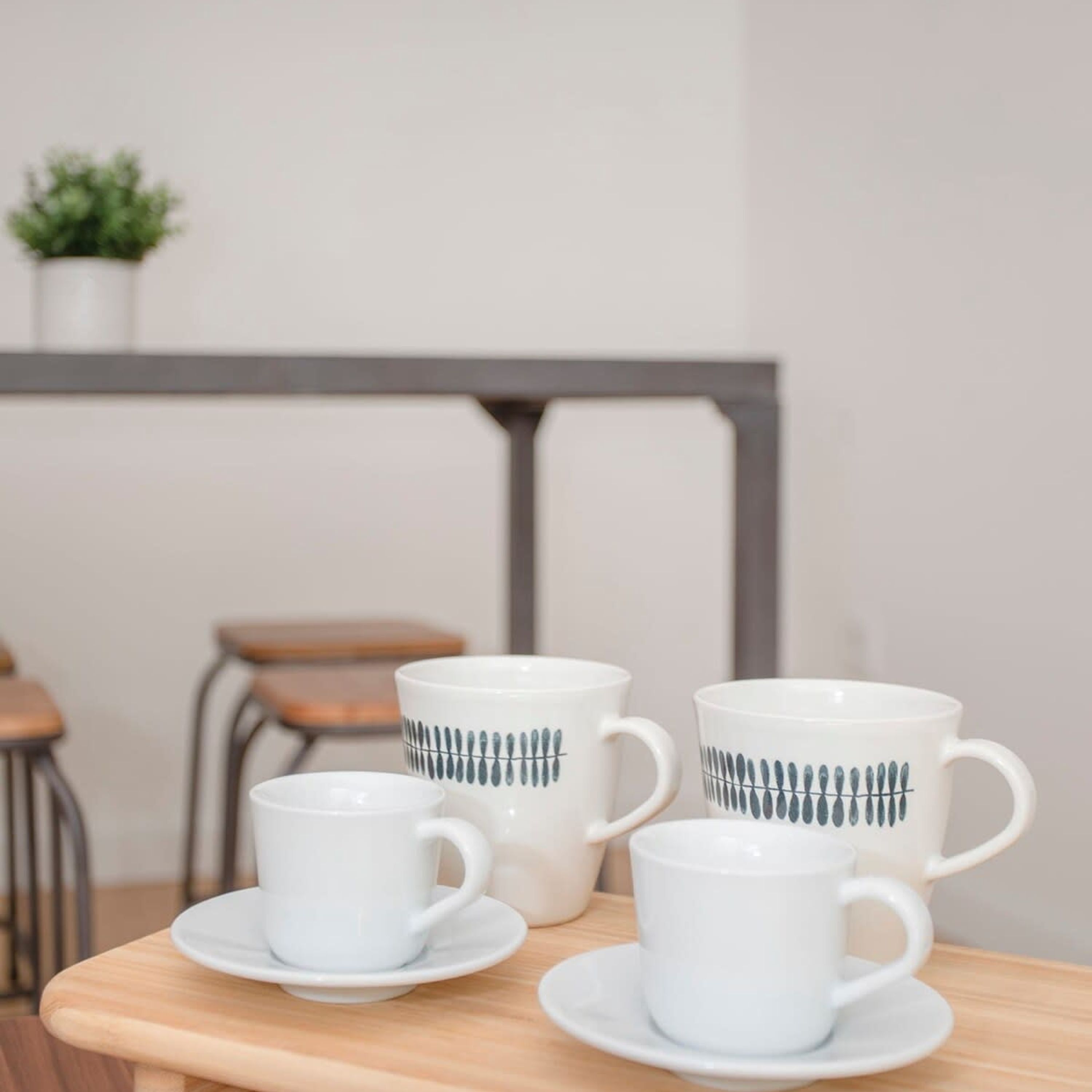A table with four white ceramic cups and saucers, each with a blue pattern, and a small potted plant in the background.