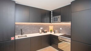 A modern kitchen with dark cabinetry, a built-in microwave, a sink, and a countertop with a kettle and toaster. - NAX Apartment D by Liiiving (Porto)