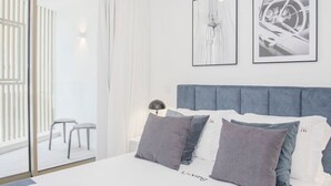 A modern hotel room with a large bed, grey and white bedding, two framed artworks on the wall, and a view of the outdoor area through a sliding glass door. - NAX Apartment D by Liiiving (Porto)
