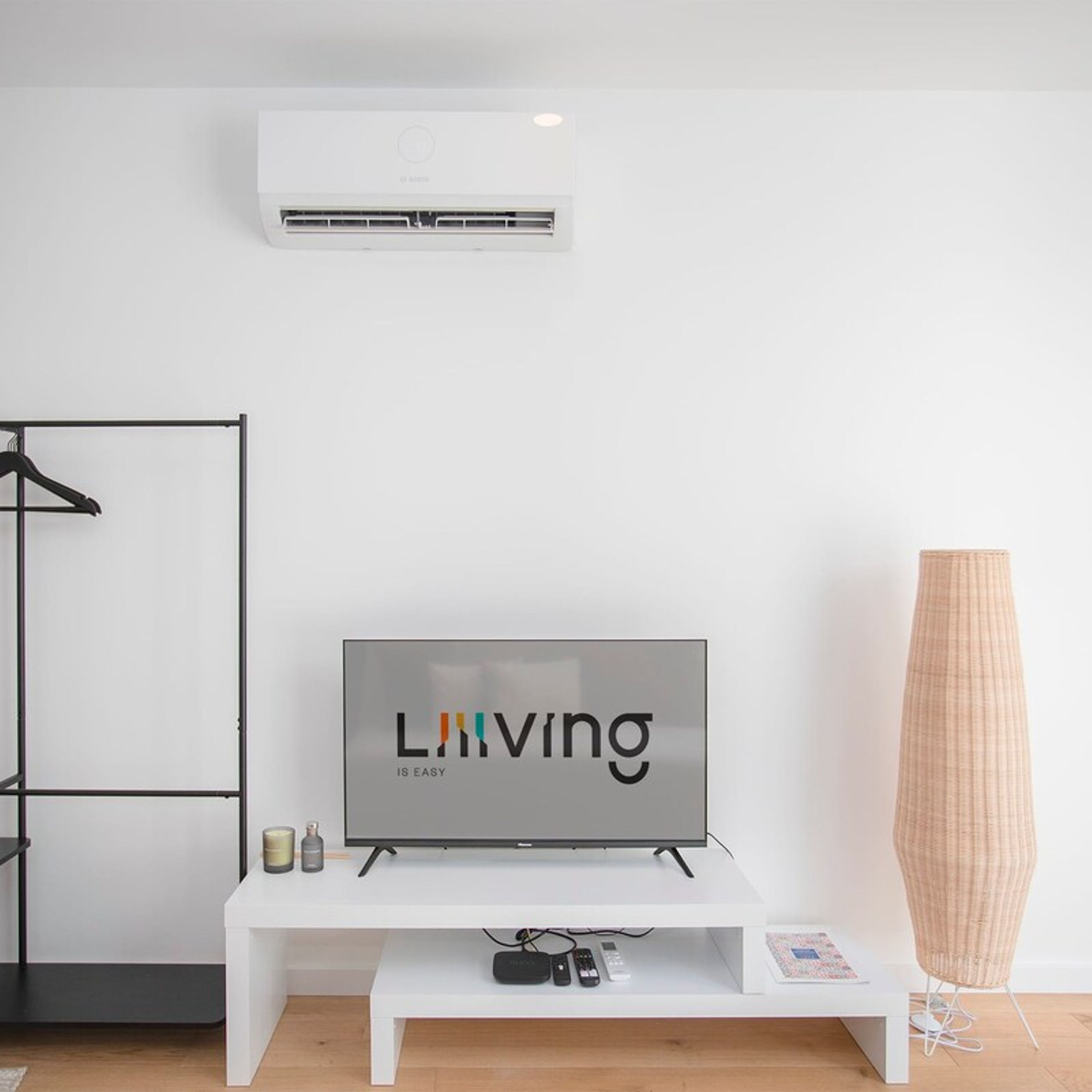 A modern living room with a flat-screen TV on a white stand, a large vase, and a wall-mounted air conditioner.