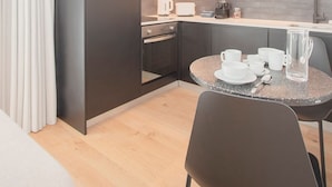 Eine moderne Küche mit dunklen Schränken, einer Mikrowelle, einer Kaffeemaschine und einem runden Tisch mit Tassen und einer Kanne.
