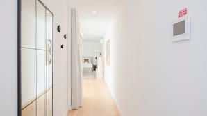 Ein moderner Flur mit Holzboden, einem großen Spiegel links und einer Tür zum Schlafzimmer.