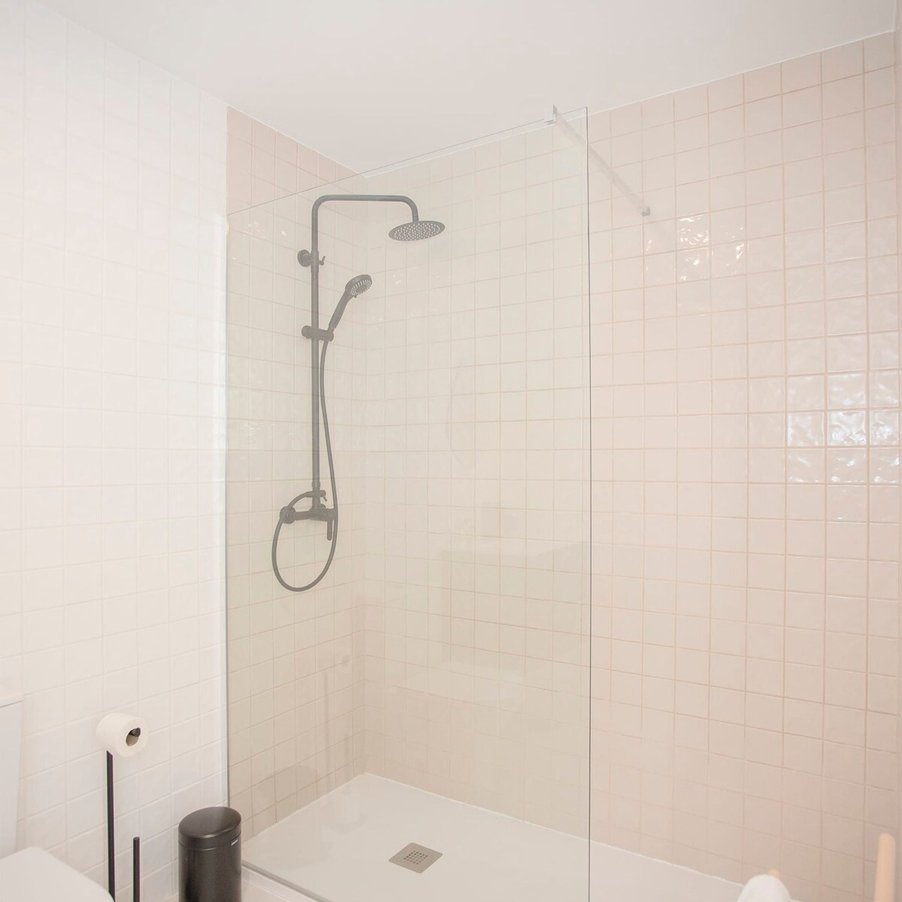 A glass-enclosed shower area with a handheld showerhead and a wall-mounted faucet.