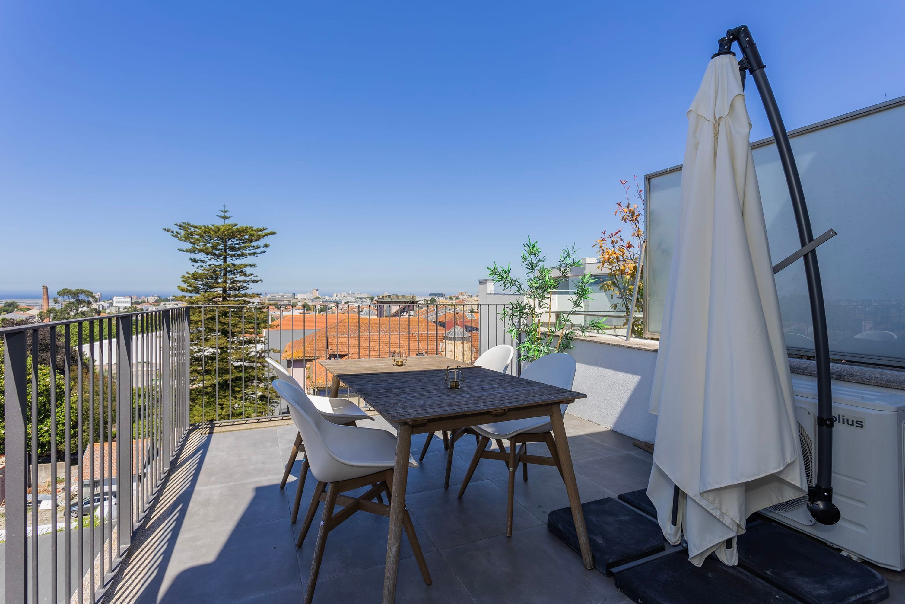 Ein Balkon mit Tisch und Stühlen, einem weißen Sonnenschirm und Blick auf Stadt und Meer.