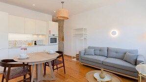 Una cocina moderna con armarios blancos, una pared de acento de piedra, una mesa de comedor con sillas y un sofá gris en una sala de estar.