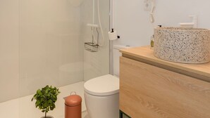 Un baño moderno con cabina de ducha de vidrio, un espejo redondo, un mueble de tocador de madera y un inodoro.