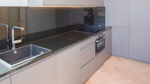 Eine moderne Küche mit schwarzem Arbeitsplatz, Spüle aus Edelstahl und eingebautem Backofen.