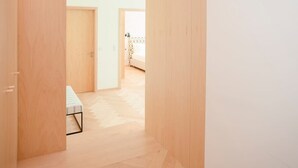 Ein Korridor mit Holzwänden und -böden, der zu einem Zimmer mit einem Bett und einem gemusterten Vorhang führt.