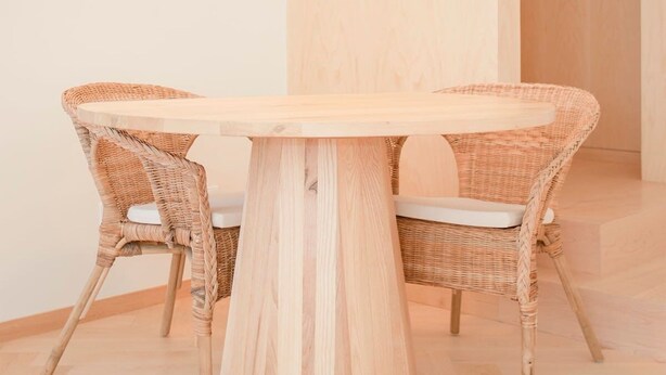 Ein runder Holztisch mit zwei Korbstühlen, einer grünen Pendelleuchte und einem Holzboden.