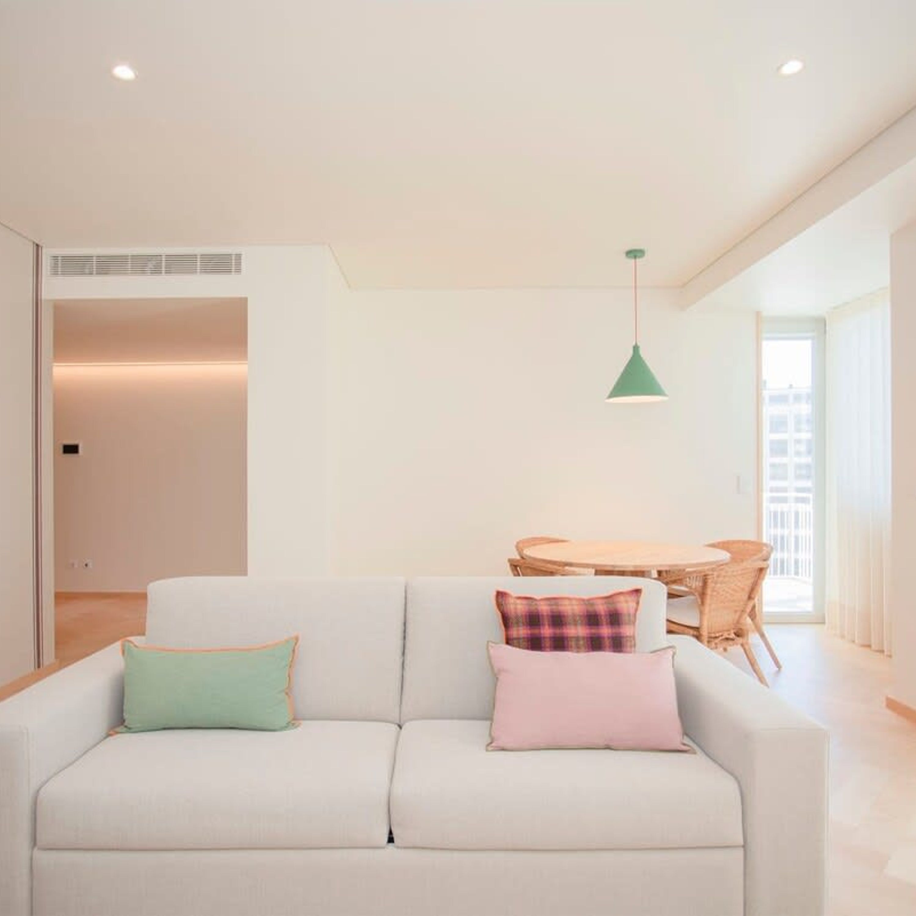 A modern living room with a white sofa, a small round table, and a hanging green pendant light.