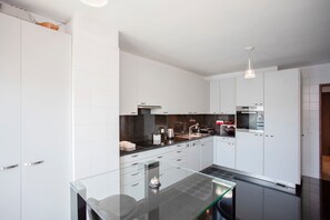 A modern kitchen with white cabinets, a glass dining table, and a pendant light. - Liiiving in Porto - Douro Riverside Apartment (Gondomar)