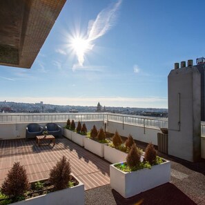 Terraço no telhado com vista para o horizonte urbano, duas cadeiras de descanso e um deck de madeira.