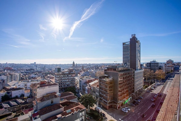 Uma paisagem urbana com um edifício alto em destaque, céu claro e sol brilhando.