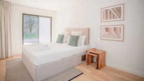 Ein modernes Schlafzimmer mit einem großen Bett, einem Nachttisch aus Holz und zwei gerahmten Bildern an der Wand.