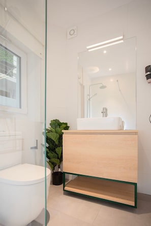 A modern bathroom with a white toilet, a wooden vanity with a mirror, and a potted plant.