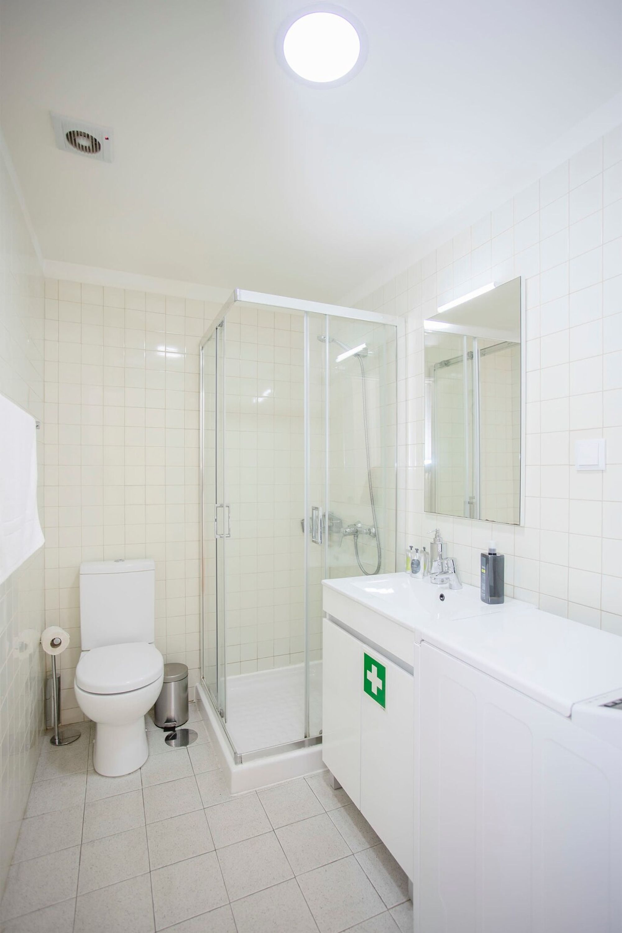 A bathroom with a toilet, a sink, a mirror, and a shower enclosure.