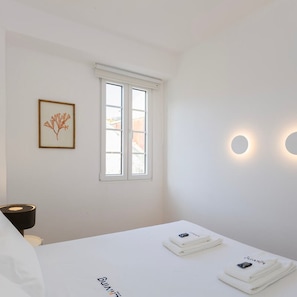 A minimalist bedroom with a bed, a framed picture, a window, and wall-mounted lights.