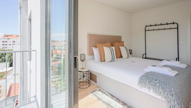 A bedroom with a bed, a bedside table, a window, and a view of buildings. - Liiiving in Porto - City Design Apartment Q (Porto)
